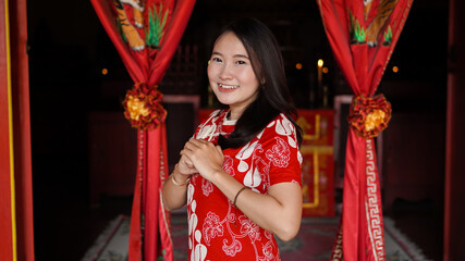 Fototapeta na wymiar Asian Chinese woman in a cheongsam dress with congratulations gest at vihara