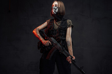 Fototapeta na wymiar Dressed in dark armour and shirt female soldier with short haircut and weared with mask poses holding ak74 rifle.