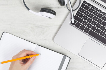 Laptop. keyboard and headphones on grey wooden desk. hand with pencil and notebook. Helpdesk or...