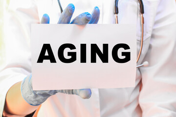 The doctor's blue - gloved hands show the word AGING - . a gloved hand on a white background. Medical concept. the medicine