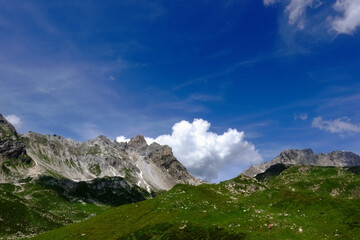 Fototapeta na wymiar high rocky mountains with a green meadow and blue sky