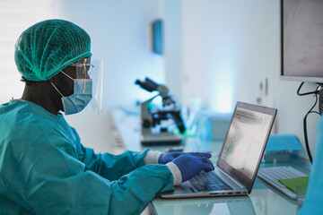 African male doctor working with laptop and protective face mask for coronavirus outbreak - Health...