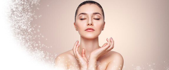 Young beautiful woman over beige background with snow and snowflakes. Cryolifting concept.