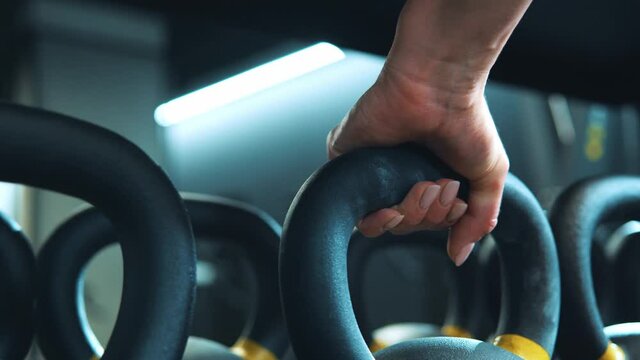 Cropped view of woman in sportswear taking a walk in the cross fit gym and looking at kettlebell on shelf. Fitness female getting ready for intense crossfit workout while taking kettlebell from shelf