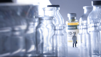 View of a man (figurine) standing and looking ahead against variety of Coronavirus COVID-19 vaccine vials with sun ray.Medical and Business concept.