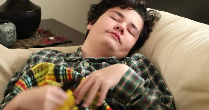 Sleepy teenage boy in pajamas lying on sofa and yawning