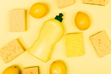 Top view of whole lemons near sponges and dishwashing liquid on yellow background