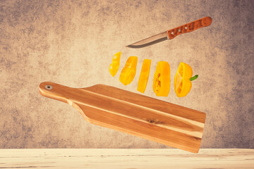Ein in Scheiben geschnittener gelber Paprika mit einem Messer und einem Schneidebrett über einem Holztisch