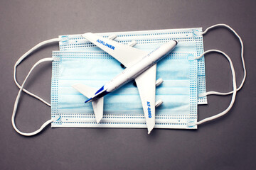 Travel and health concept. Model of a white plastic airplane and masks on grey background.