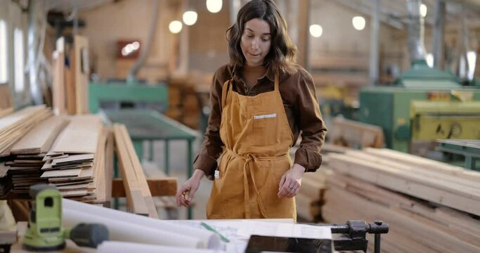 Female carpentry worker having some paper work with drawings at the table in the joinery manufacturing. Woodwork designing and craft production concept