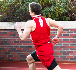 Runner racing fast on a track next to brick wall