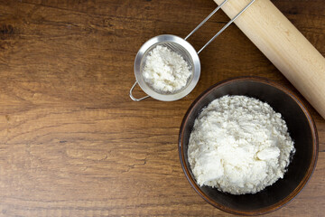 Flour in a wooden bowl, a small sieve and cinnamon sticks on a wooden table. Side view with copy space. Kitchen baking tools with place for text, or logo.