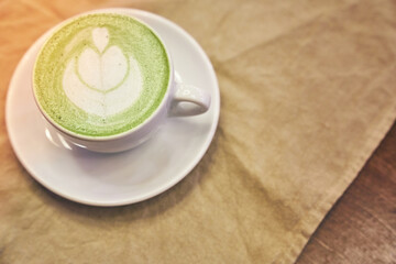 Cup of matcha latte on wooden background and a beige napkin in a cafe with copy space. High quality photo