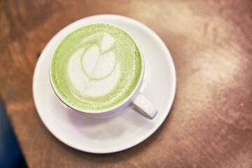Cup of matcha latte on wooden background and napkin in a cafe with copy space