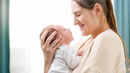 Portrait of 2 weeks old little baby boy with young caring mother against big window at house. Concept of family happiness and loving parents with little children