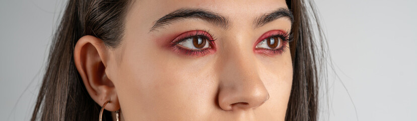 Obraz premium Macro shot of female eyes with red eyeshadow make-up. Close-up of woman eyelashes. Panoramic shot. High quality image. Panorama banner.