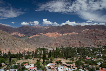Obraz premium Tilcara village at the foot of the mountains. Panorama view of the colorful mountains and town buildings under a beautiful sky with clouds.