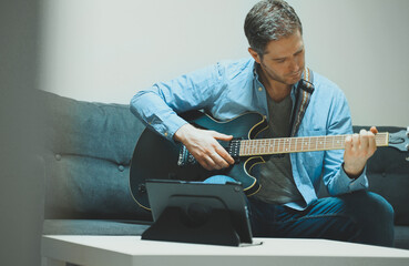 Man learns how to play the guitar. Remote online lesson.