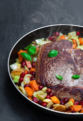 Braised beef with cranberries and vegetables on black stone background