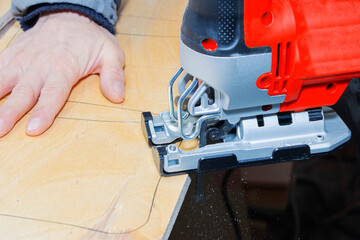 young man carpenter builder working with electric jigsaw and wood.