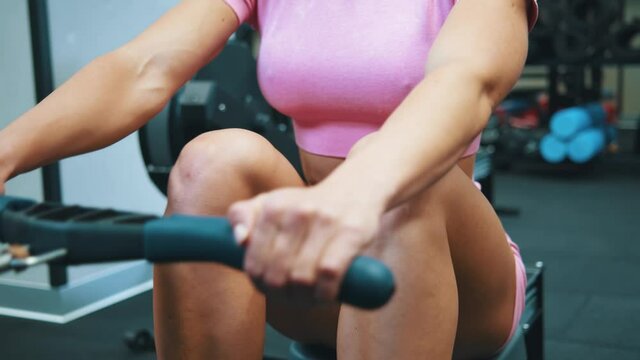 Cropped view of the muscular sporty woman workout on training simulator in crossfit gym. Strong bodybuilder woman training with rowing machine to improve her body. Sport and recreation concept