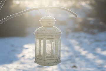 Lamp in snow. Candle lantern with frosty pattern hanging on a branch in the sun. Shallow depth of field 