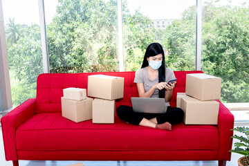 Asian attractive woman, Entrepreneurs, wearing surgical masks start their own small business at home By trading Through the online channel,  to SME e-commerce and new normal concept
