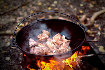 Cooking pilaf in Asian cauldron on the grill outside in forest. Selected focus.