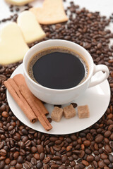 Tasty coffee with cinnamon and beans in cup on light background