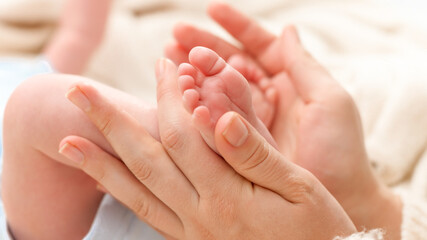 Closeup shot of young mother gently holding and touching little feet of her newborn baby boy lying in bed. Concept of family happiness and loving parents with little children