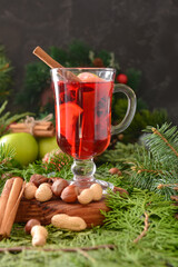 Tasty mulled wine with cinnamon in glass on Christmas tree branches