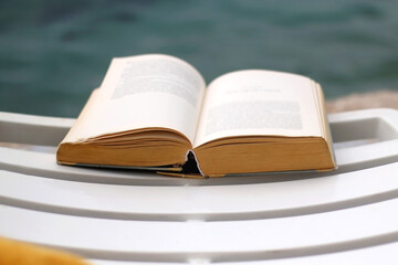 Open book on the deck chair by the water. Selective focus.