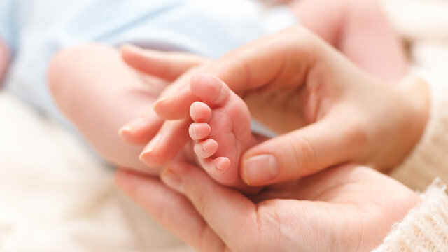 Closeup image of mother massaging little feet of her newborn baby boy lying on bed