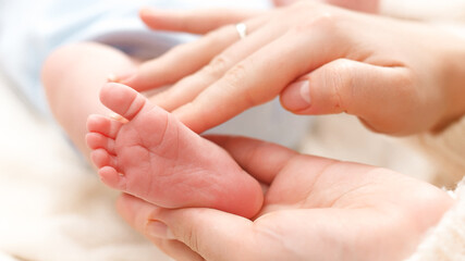 Closeup shot of mother touching and stroking little feet of her newborn baby. Concept of family happiness and loving parents with little children. Baby massage and healthcare