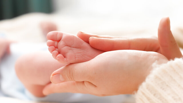 Tiny baby feet in female hands. Young mother gently touching and stroking her newborn baby legs. Concept of family happiness and loving parents with little children.