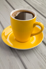 Black  coffee in the yellow cup on the gray wooden surface
