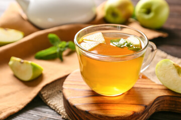 Cup of hot tea with apples and mint on wooden board