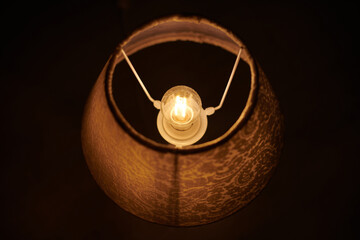 Incandescent lamp in round lampshade glowing in dark.