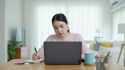 Candid young attractive asian female employee wear earphone listen to digital online course development program in quarantine social distance at home reskill upskill school class for career path.