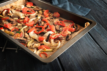 Healthy oven vegetables such as bell pepper, tomato, zucchini, mushroom, fennel and eggplant on a baking tray on dark rustic wood, selected focus