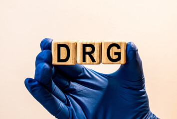 The word DRG which is made from wooden cubes. Hands in a blue glove. Isolated on WHITE background.