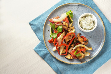 Baked oven vegetables such as bell pepper, tomato, zucchini, mushroom, fennel and eggplant and dip on a blue plate , white wooden table with copy space, high angle view from above