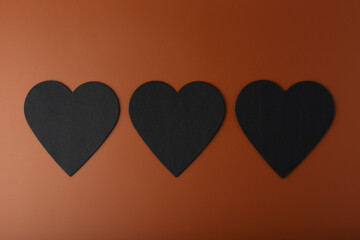 Flat lay with three black hearts on brown background. Concept of love and relationship