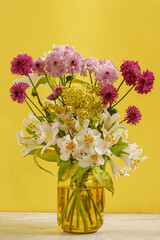 Florero amarillo con flores de diferentes tipos y colores sobre una mesa con pared amarilla. Concepto decoración de interiores
