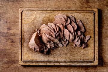 Baked beef tongue sliced, serving on wooden cutting board over wood background. Flat lay.