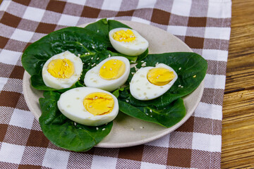 Boiled eggs with fresh spinach leaves and sesame seeds on wooden table