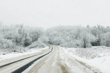 A snow-covered road through a snow-white forest covered with snow on a frosty day.