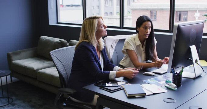 Diverse businesswomen using computer and discussing at desk in office