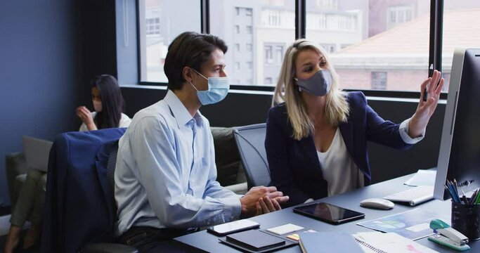 Diverse business people wearing face masks using computer in office