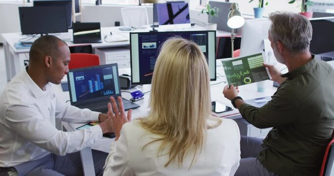Diverse business people sitting using computer and takling at desk in office